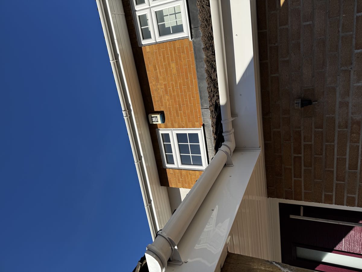 Freshly cleaned white gutter and fascia against a blue sky
